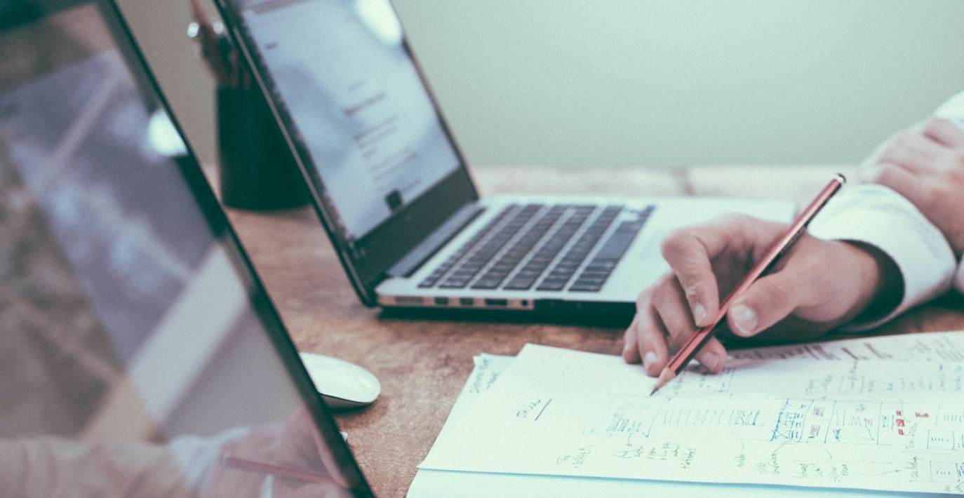 person writing in a notebook while looking at financials on a laptop